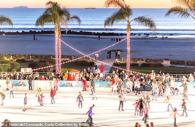 A crowd skates on an outdoor ice rink by the beach at sunset, with palm trees, twinkling lights, and the ocean in the background. People watch from the sidelines and walk along the beachfront path.