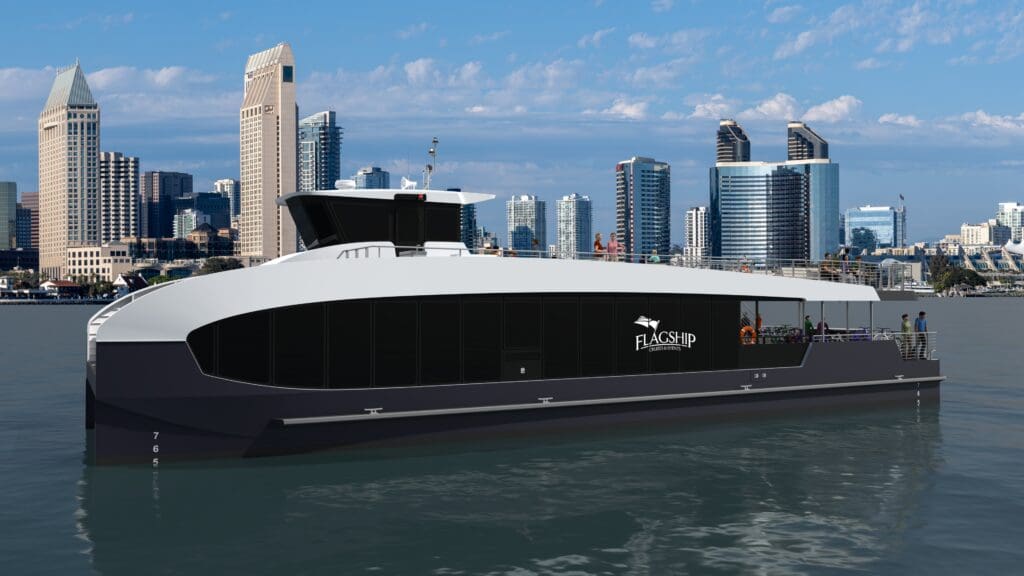 A modern, black and white passenger ferry with the “Flagship” logo floats on calm water, with a city skyline featuring tall buildings and a blue sky with scattered clouds in the background.