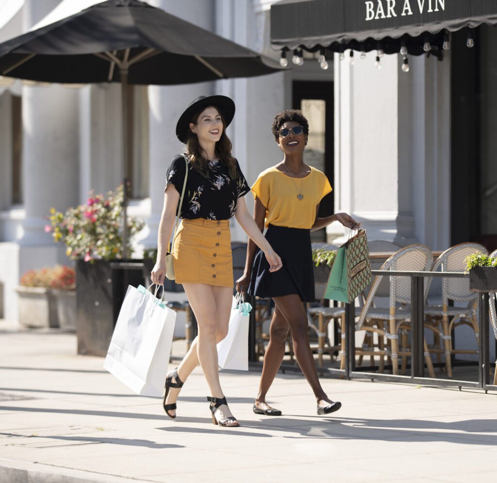 two women smiling and walking as they hold shopping bags walking down orange avenue in coronado